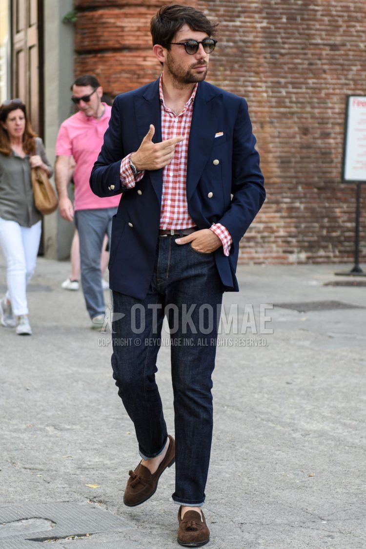 A spring/summer/fall men's coordinate outfit with plain black sunglasses, plain navy tailored jacket, white/red checked shirt, plain brown leather belt, plain navy denim/jeans, and suede brown tassel loafer leather shoes.