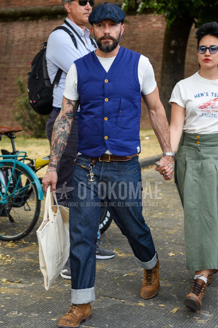 Other solid navy, solid blue gilet, solid white t-shirt, solid brown leather belt, solid navy denim/jeans, and brown work boots for a summer men's outfit.