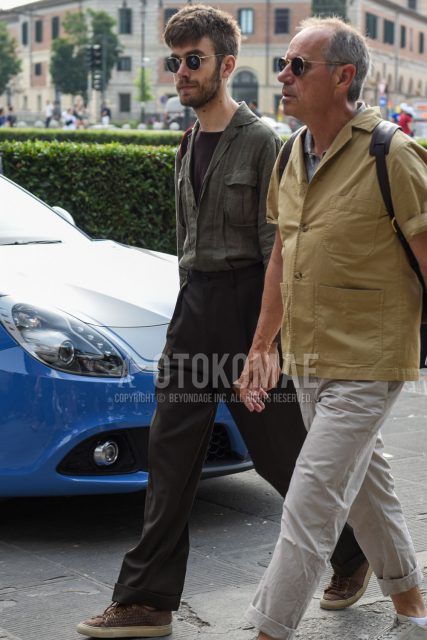 A spring/summer men's coordinate outfit with round black/gold solid sunglasses, linen olive green solid shirt, brown solid t-shirt, gray solid slacks, solid pleated pants, and brown low-cut sneakers.
