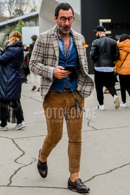 Winter/fall men's coordinate outfit with plain glasses, brown checked tailored jacket, plain navy gilet, plain blue denim/chambray shirt, black dotted leather belt, plain brown winter pants (corduroy, velour), brown other loafer leather shoes.