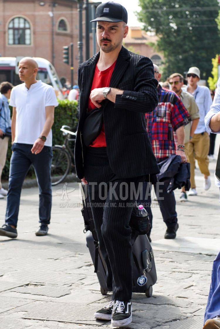 Spring and fall men's coordinate outfit with plain black baseball cap, plain red t-shirt, black low-cut sneakers from Vans, plain black body bag, and black striped suit.