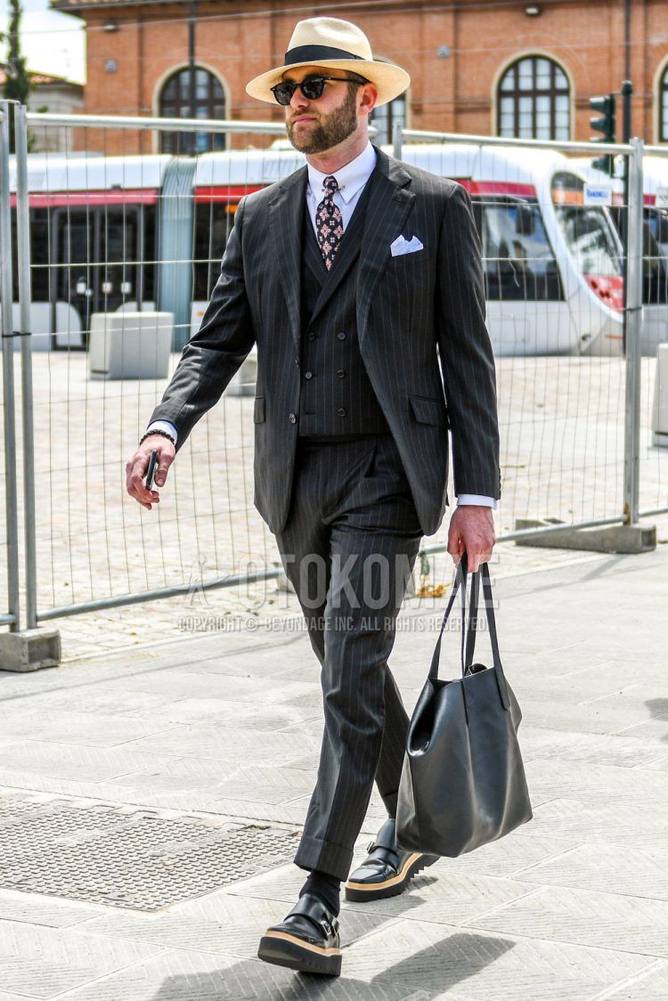 Spring, summer and fall men's coordinate outfit with solid beige hat, solid black sunglasses, solid white shirt, solid black socks, black monk shoes leather shoes, solid gray tote bag, black striped three-piece suit and black other tie.