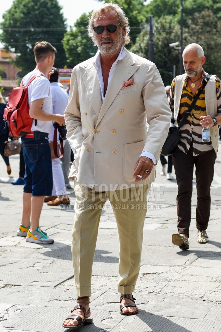 Spring, summer and fall men's coordinate outfit with brown tortoiseshell sunglasses, plain beige tailored jacket, plain white shirt, plain beige slacks and brown leather sandals.