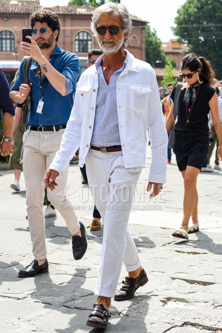 A spring and fall men's outfit with beige tortoiseshell sunglasses, plain white denim jacket, light blue striped shirt, plain brown leather belt, plain white slacks, plain cotton pants, and brown monk shoe leather shoes.