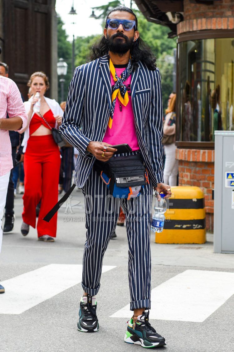 Spring, summer and fall men's coordinate outfit with plain blue/black sunglasses, orange/navy other scarf/stall, plain pink t-shirt, multi-colored low-cut sneakers, multi-colored plain body bag and white/navy striped suit.