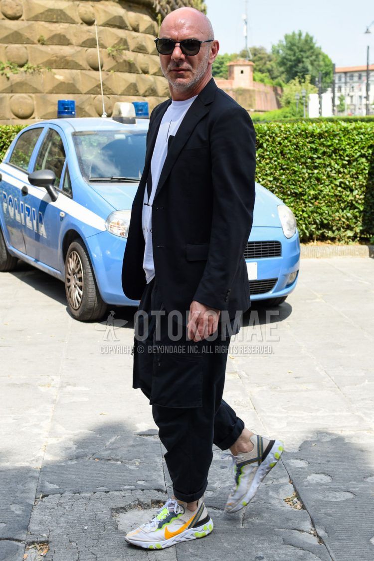 A men's spring/summer/fall coordinate outfit with plain black sunglasses, plain black tailored jacket, plain white t-shirt, plain black cargo pants, and Nike React Element multi-colored low-cut sneakers.