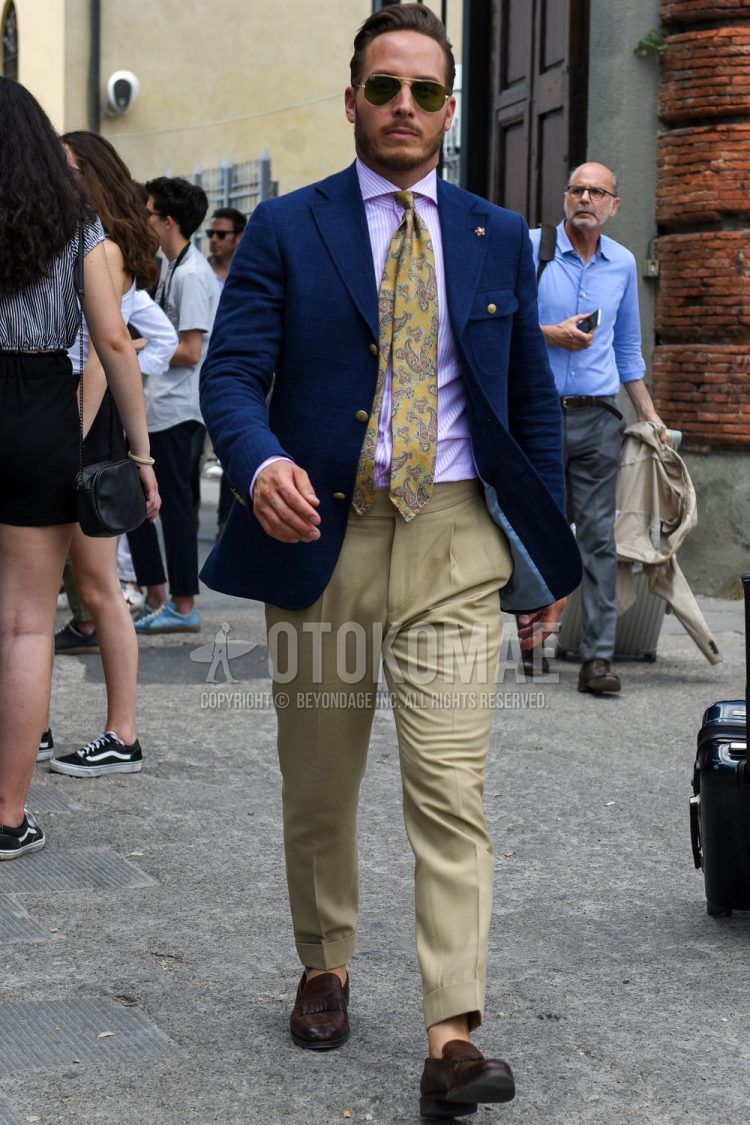 A men's spring/summer/fall outfit for men with gold/black solid sunglasses, navy solid tailored jacket, pink solid shirt, beige solid beltless pants, brown coin loafer leather shoes, and beige paisley tie.