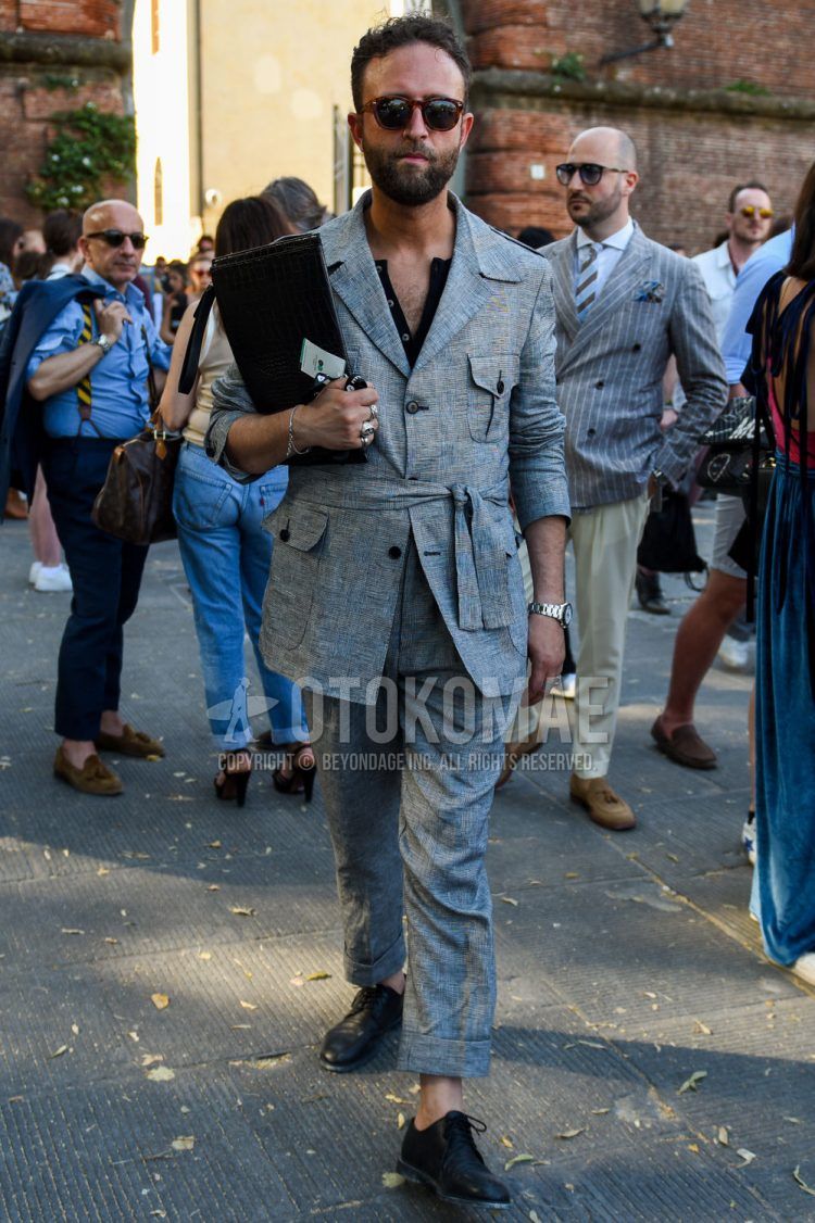 Men's spring/fall outfit with brown tortoiseshell sunglasses in Boston, plain gray safari jacket, plain black t-shirt with henley neck tee, plain gray slacks, black plain toe leather shoes, and plain black clutch/second bag/drawstring.