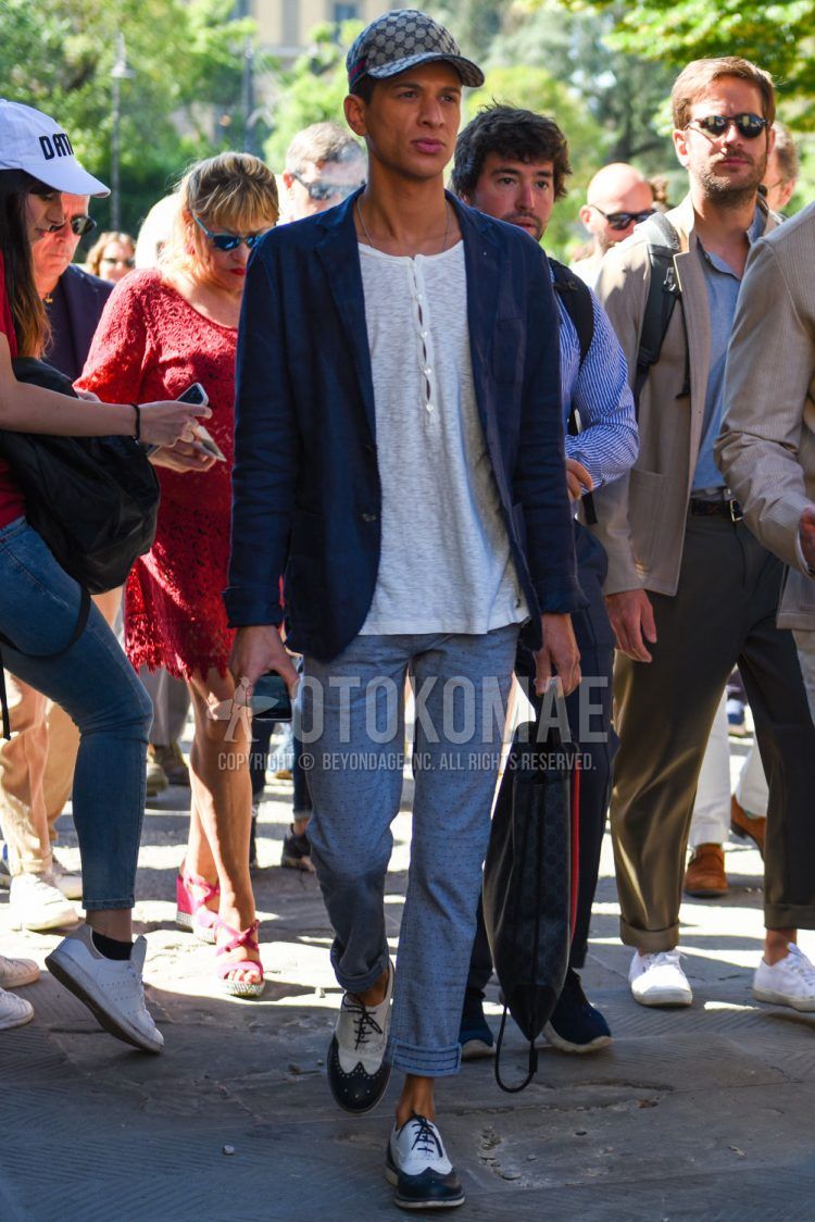 Gucci beige other baseball cap, plain navy tailored jacket, plain white t-shirt with henley neck, plain gray slacks, and white/black wingtip leather shoes for men's spring/summer outfits.