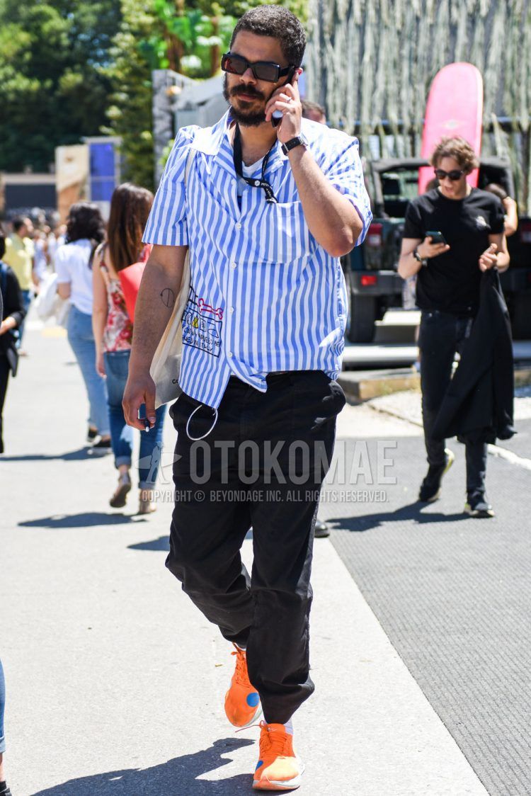 A summer men's coordinate outfit with plain black sunglasses, a short-sleeved light blue striped shirt, plain black cotton pants, and Nike Off-White The Ten Zoom Fly Mercurial orange low-cut sneakers.