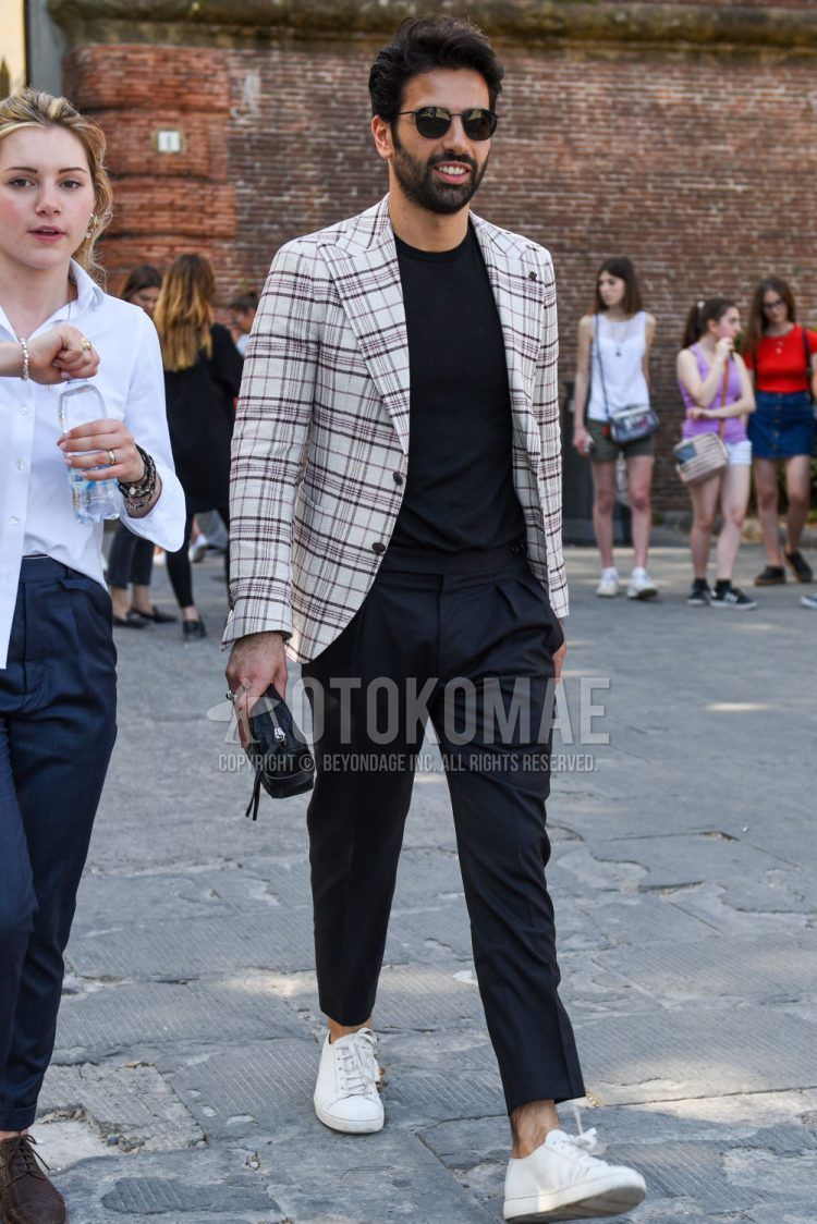 A men's spring/summer/fall outfit for men with plain black sunglasses, beige checked tailored jacket, plain black t-shirt, plain black slacks, white low-cut sneakers, and plain black clutch bag/second bag/drawstring.