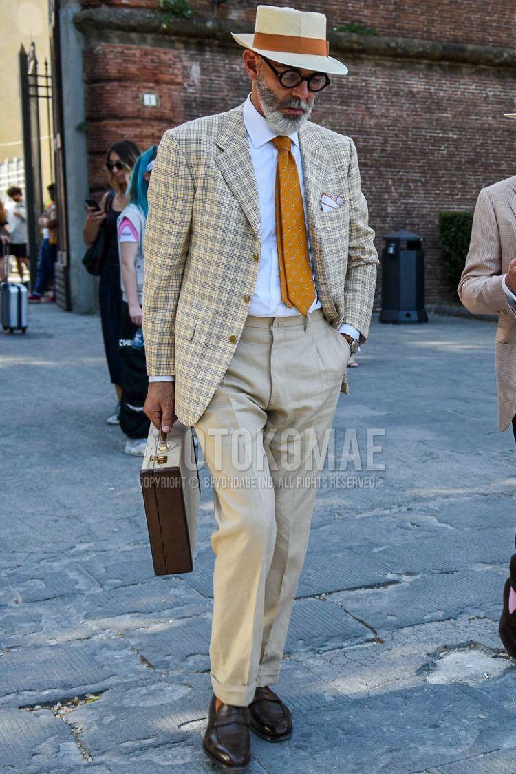 A solid beige hat, solid black glasses, beige checked tailored jacket, solid white shirt, solid beige slacks, brown coin loafer leather shoes, solid brown briefcase/handbag, and orange regimental tie for men's spring/summer/fall Outfit.