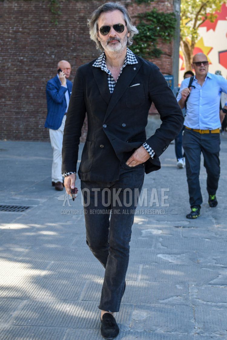A spring/summer/fall men's coordinate outfit with plain black sunglasses, a plain black tailored jacket by Tagliatore, a black/white checked shirt, plain black denim/jeans, and black tassel loafer leather shoes.