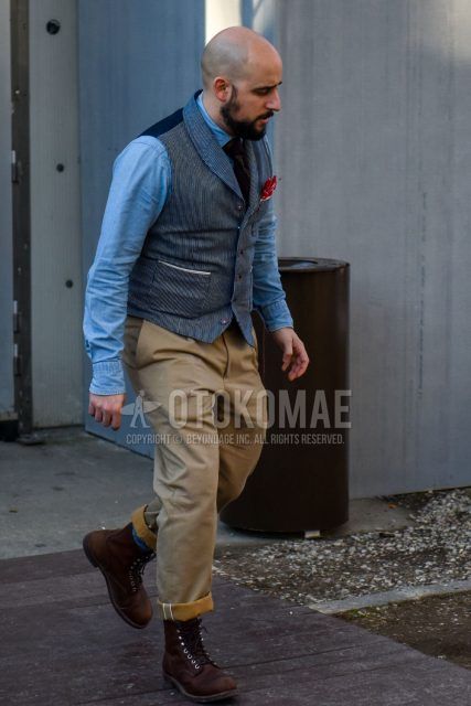 Winter men's outfit with a solid light blue denim/chambray shirt, solid blue gilet, solid beige chinos, brown work boots, and solid navy tie.