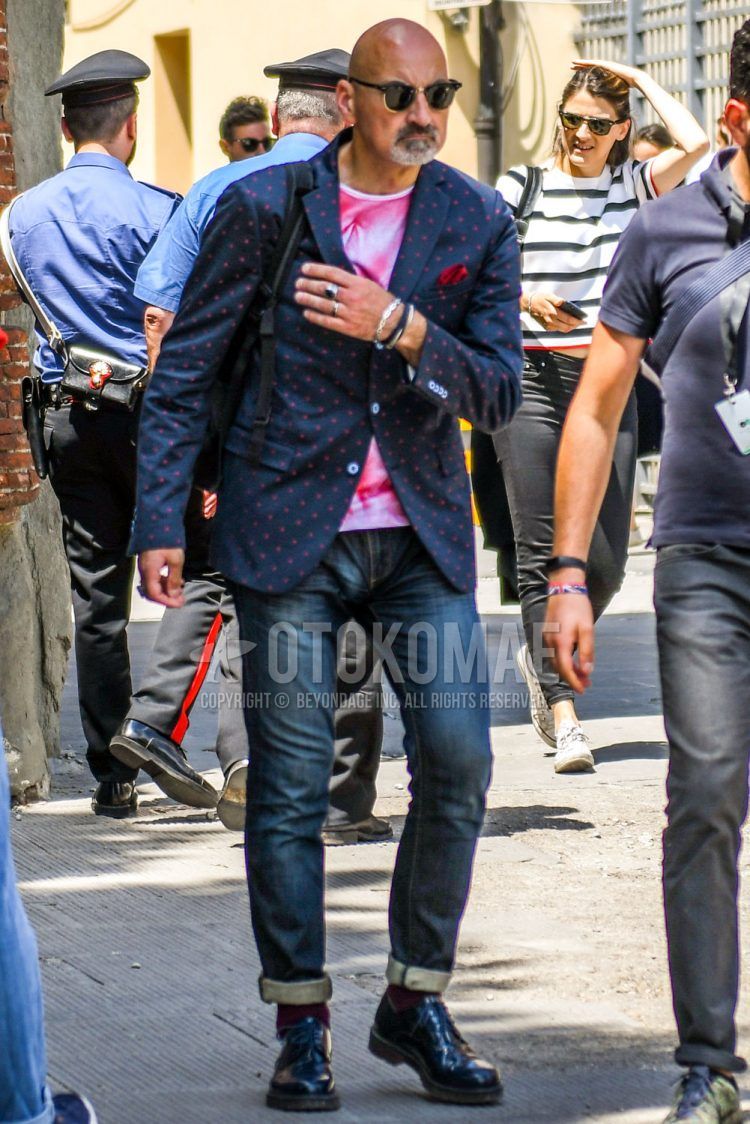 Spring/Summer/Fall men's coordinate outfit with gold solid sunglasses, navy/red dot tailored jacket, white/pink botanical t-shirt, blue solid denim/jeans, red solid socks, black other leather shoes.