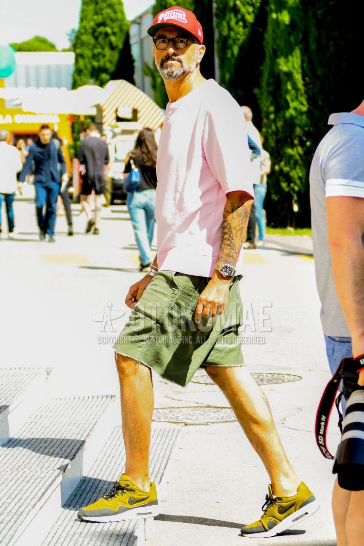 A men's spring/summer coordinate outfit with a solid color baseball cap, a solid color pink t-shirt, solid color olive green shorts, and yellow-cut sneakers.