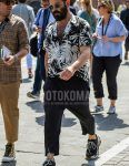 A summer men's coordinate outfit with plain silver sunglasses, a black/white botanical shirt, plain black ankle pants, and Balenciaga black low-cut sneakers.