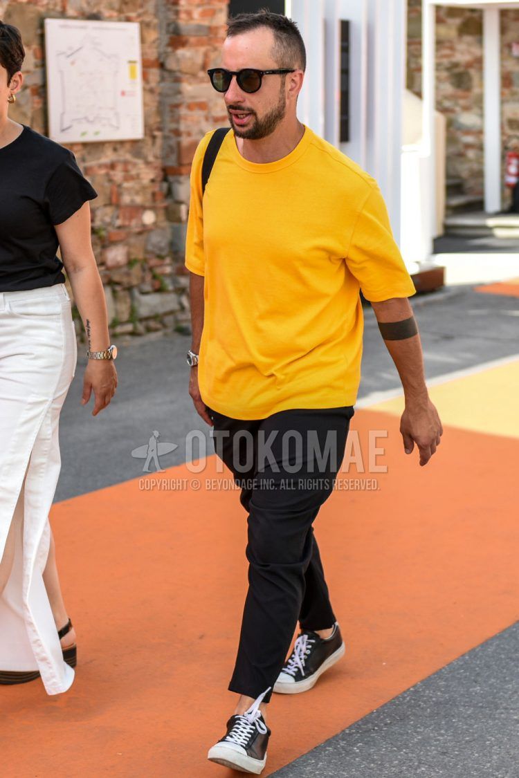 A summer men's coordinate outfit with plain black sunglasses, plain yellow t-shirt, plain black ankle pants, and black low-cut sneakers.