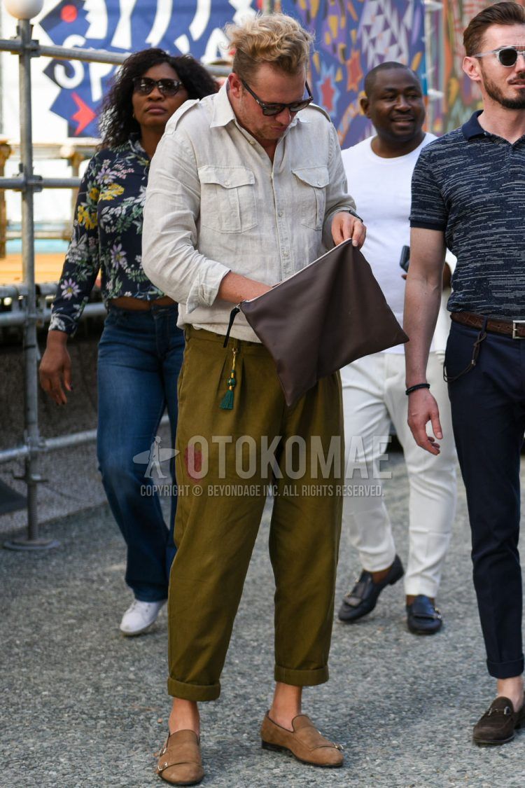 A summer men's coordinate outfit with plain black sunglasses, plain white shirt, plain olive green beltless pants, beige other loafer leather shoes, and plain brown clutch/second bag/drawstring bag.