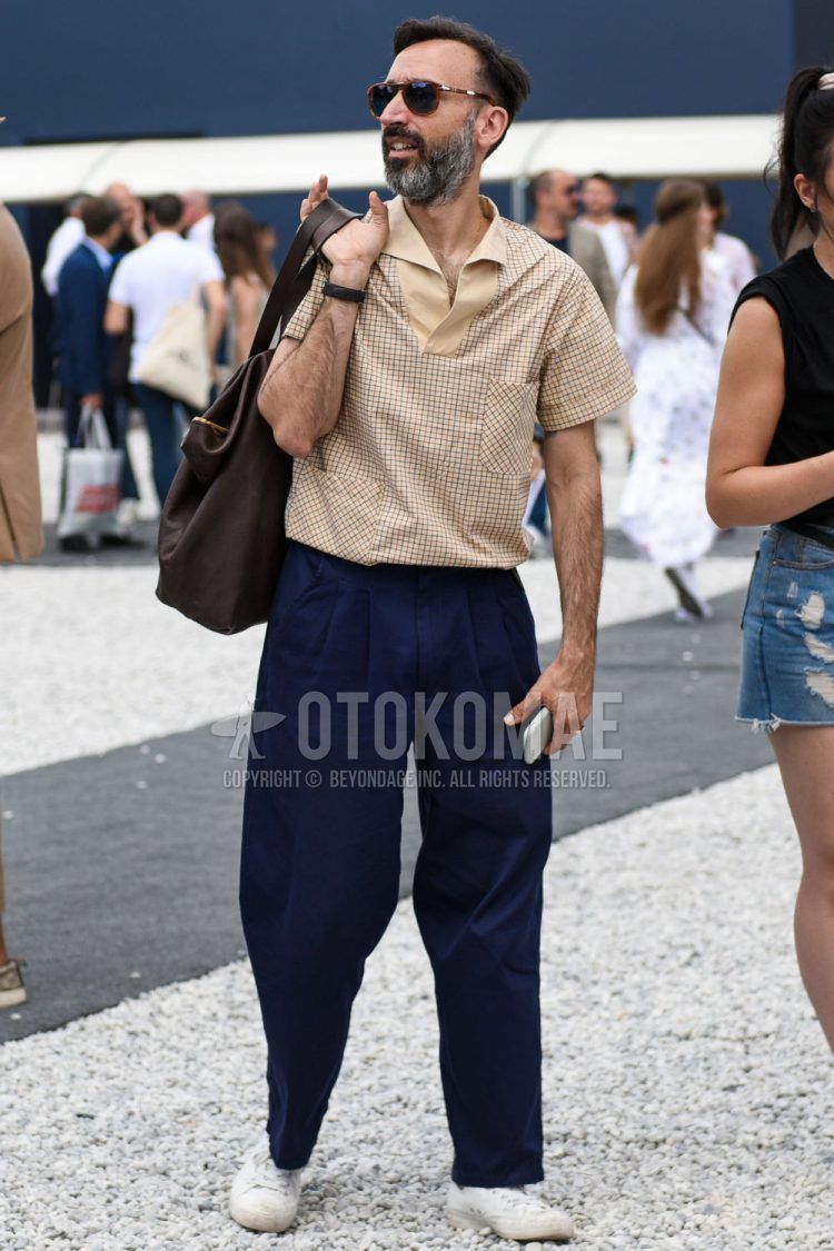 A summer men's outfit with brown tortoiseshell sunglasses, beige checked shirt, plain navy wide pants, plain chinos, plain pleated pants, white low-cut sneakers, and plain brown briefcase/handbag.