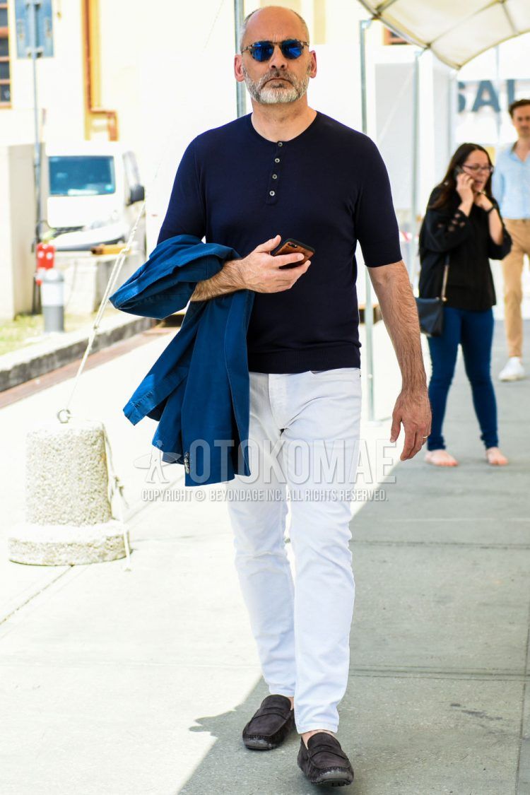 Summer men's coordinate outfit with blue/beige tortoiseshell sunglasses, plain black t-shirt with henley neck, plain white denim/jeans, and suede blue moccasins/deck shoes leather shoes.