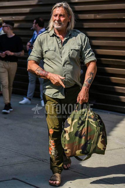 Spring, summer and fall men's coordinate outfit with olive green solid shirt, olive green other jogger pants/ribbed pants, brown leather sandals and green camouflage Boston bag.