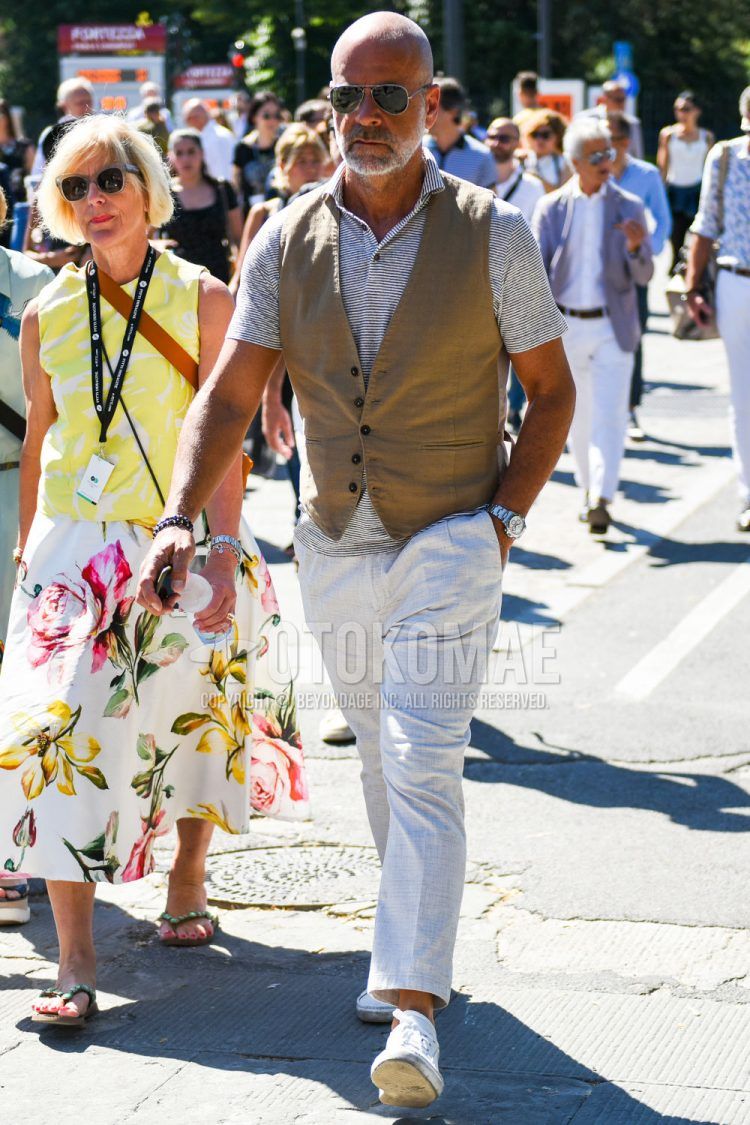 Teardrop Ray-Ban aviators with plain black and gray sunglasses, plain beige gilet, black and white striped polo shirt, plain gold slacks, plain pleated pants, plain ankle pants, and white low-cut sneakers for men's spring and summer outfits.