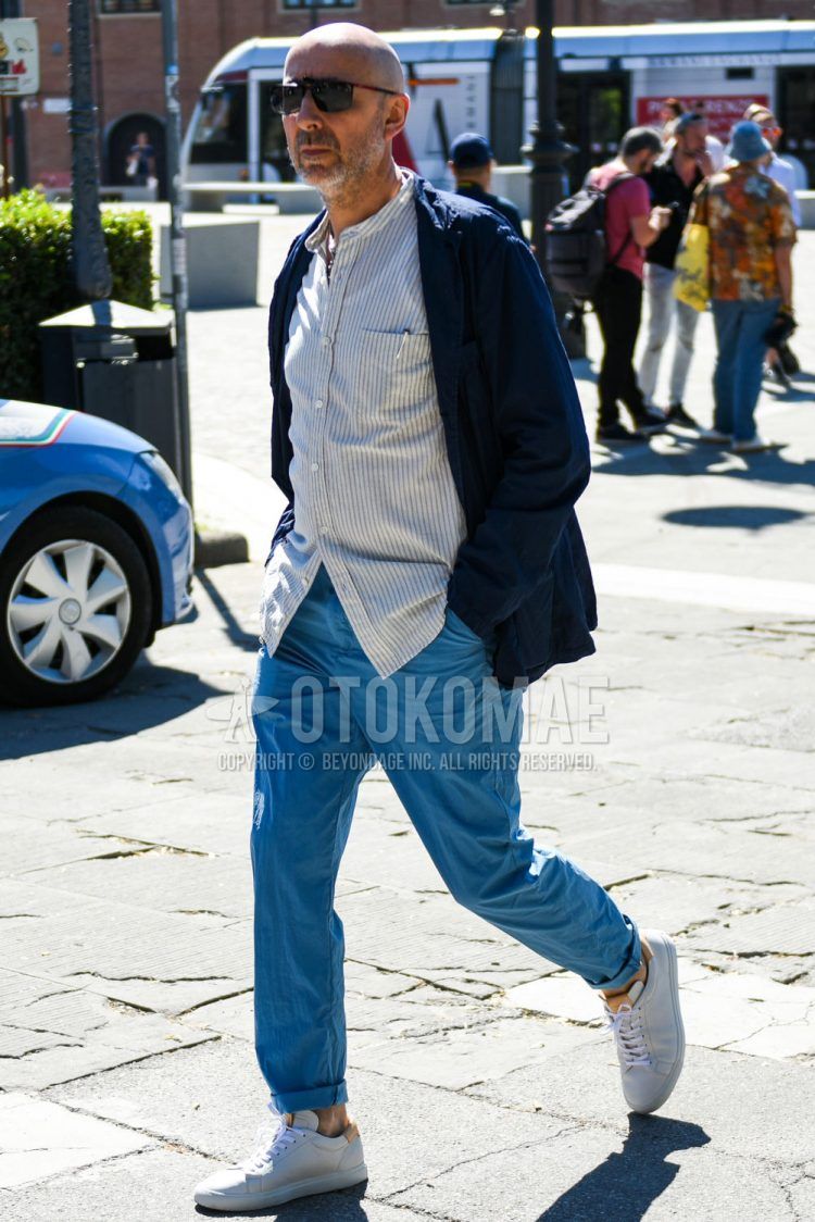 Spring and fall men's coordinate outfit with plain black/red sunglasses, plain navy tailored jacket, band collar white/gray striped shirt, plain light blue cropped pants, and white low-cut sneakers.