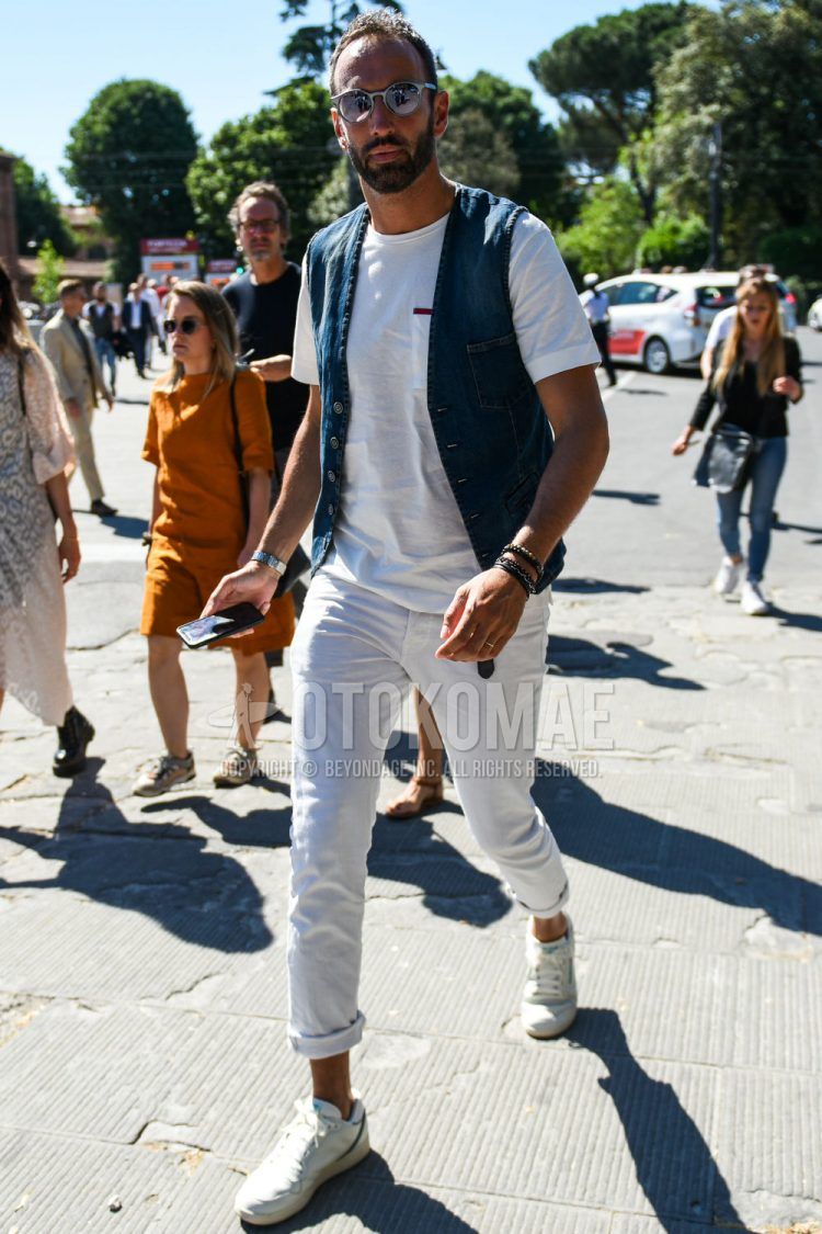 A summer men's coordinate outfit with plain gray sunglasses, plain navy gilet, plain white t-shirt, plain white cotton pants, and white low-cut Reebok sneakers.