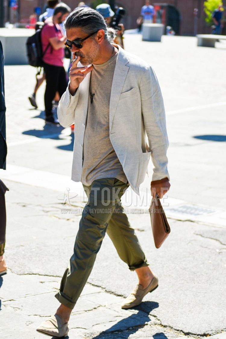 Men's spring/summer/fall outfit with brown tortoiseshell sunglasses, plain beige tailored jacket, plain beige t-shirt, plain olive green cargo pants, suede beige coin loafer leather shoes, and plain brown clutch/second bag/drawstring bag.