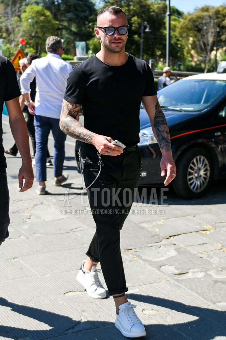 A summer men's coordinate outfit with plain black sunglasses, plain black t-shirt, plain black leather belt, plain black cotton pants, and white low-cut sneakers by Alexander McQueen.