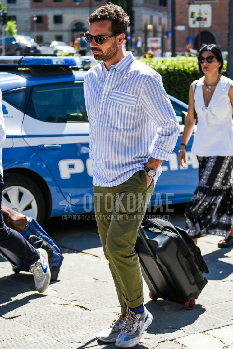 Summer/spring/fall men's coordinate outfit with black/brown tortoiseshell sunglasses, gray/white striped shirt, olive green solid color cotton pants, blue/red solid color socks, and white low-cut sneakers.