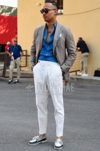 A spring/summer men's coordinate outfit with plain black sunglasses from Boston, plain beige tailored jacket, plain blue denim/chambray shirt, plain white beltless pants, plain pleated pants, and white/light blue moccasins/deck shoes leather shoes.