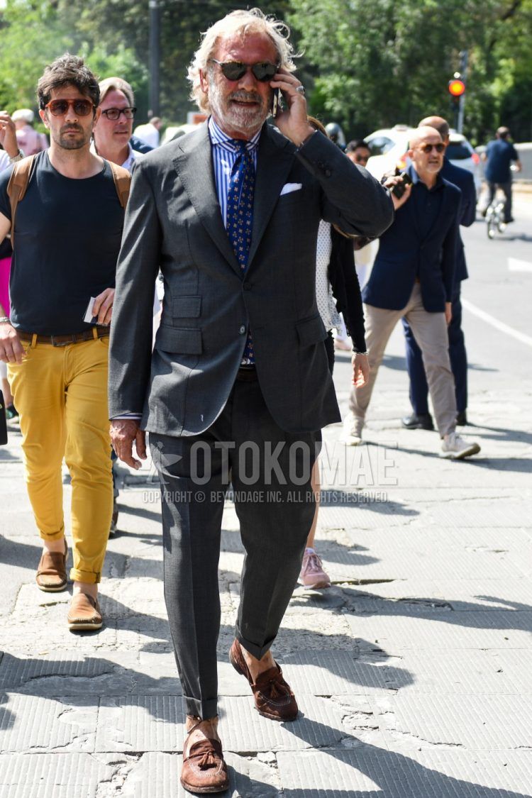 Men's spring, fall, and summer outfit with plain black sunglasses, plain blue/white shirt, brown tassel loafer leather shoes, plain dark gray suit, and blue or other tie.
