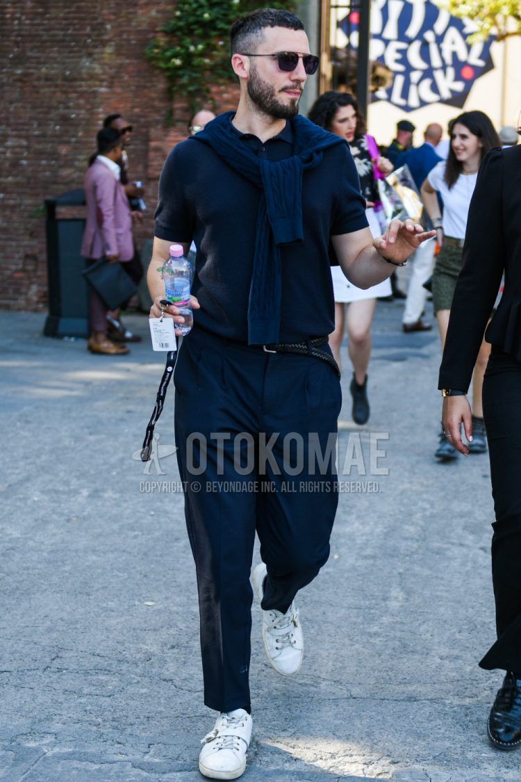 A summer men's coordinate outfit with solid color sunglasses, solid color navy polo shirt, solid color black leather belt, solid color mesh belt, dark gray solid color slacks, solid color pleated pants, and white low cut sneakers.