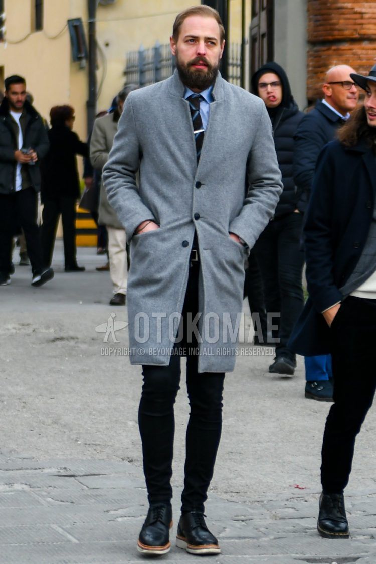 Men's fall/winter outfit with plain gray chester coat, plain light blue shirt, plain black leather belt, plain black denim/jeans, black wingtip leather shoes, and brown regimental tie.