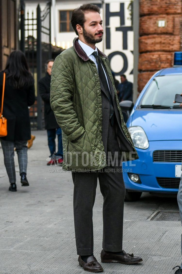 Fall and winter men's coordinate outfit with olive green solid color quilted jacket, solid color white shirt, solid color black socks, brown tassel loafer leather shoes, solid color gray suit, and gray dot tie.