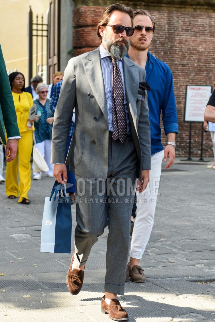 Spring and fall men's coordinate outfit with brown tortoiseshell sunglasses, plain blue/white shirt, suede brown tassel loafer leather shoes, plain gray suit, and brown dot tie.