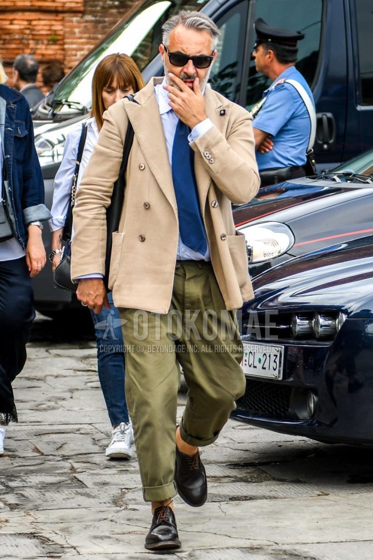 Spring and fall men's outfit with plain black sunglasses, plain beige tailored jacket, plain white shirt, plain olive green chinos, brown plain toe leather shoes, plain black shoulder bag, and plain blue tie.