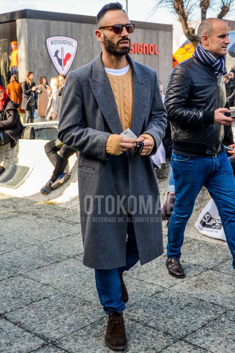 Fall/winter men's coordinate outfit with solid color sunglasses, solid color gray chester coat, solid color beige sweater, solid color blue denim/jeans, brown chukka boots, suede shoes leather shoes.