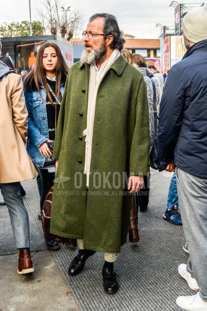 Fall/winter oversized men's outfit with plain glasses, plain white scarf/stall, plain olive green stainless steel coat, plain white shirt, plain beige chinos, plain black socks, and black monk leather shoes.