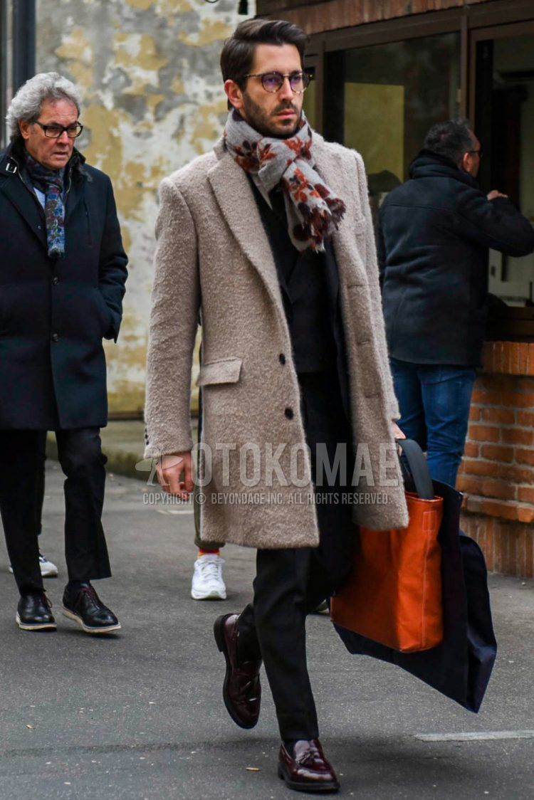 A winter men's outfit outfit with plain glasses, plain gray scarf/stall, plain beige chester coat, plain black sweater, brown tassel loafer leather shoes, plain orange tote bag, and plain gray suit.