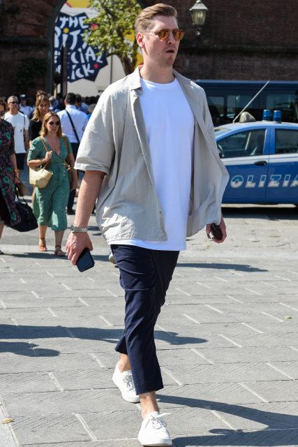 A men's oversized coordinate outfit for spring, summer, and fall with plain brown sunglasses, plain beige shirt, plain white t-shirt, plain navy cotton pants, and white low-cut sneakers.