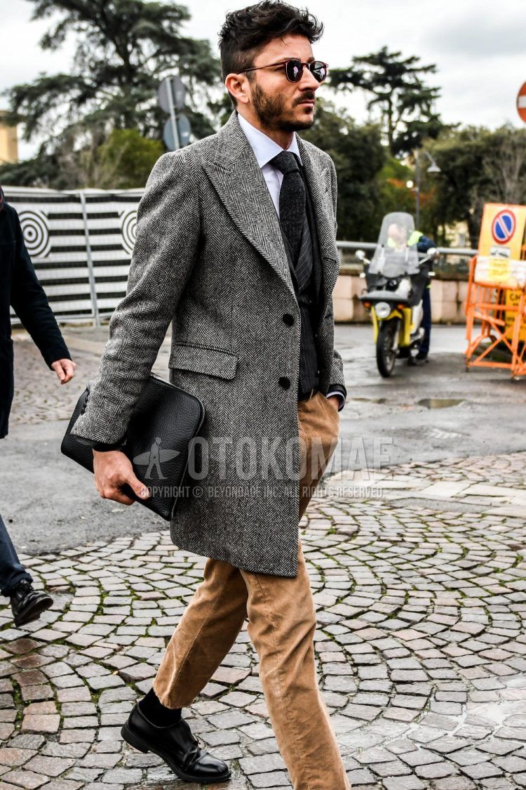 Solid color sunglasses, gray herringbone chester coat, solid color white shirt, solid color gray tailored jacket, gray striped gilet, multi-color solid color winter pants (corduroy,velour), solid color black socks, black monk shoes leather shoes, solid color black clutch bag/second bag/drawstring, and a plain gray necktie for a men's fall/winter outfit.