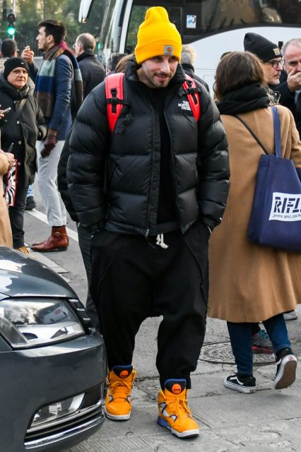 Winter men's oversized coordinate outfit with solid yellow knit cap, solid black down jacket, solid black sweater, solid black easy pants, solid black wide-leg pants, and yellow high-cut sneakers.