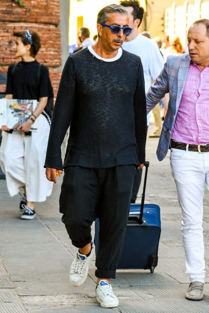 A men's oversized coordinate outfit for spring, summer, and fall with solid blue sunglasses, solid navy sweater, solid white t-shirt, wide black pants, white low-cut sneakers, and solid blue others.