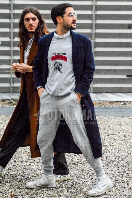Fall/winter oversized men's outfit with plain glasses, plain black chester coat, grey graphic sweatshirt, plain white shirt, plain grey sweatpants, plain jogger pants/ribbed pants, and white low-cut Reebok sneakers.