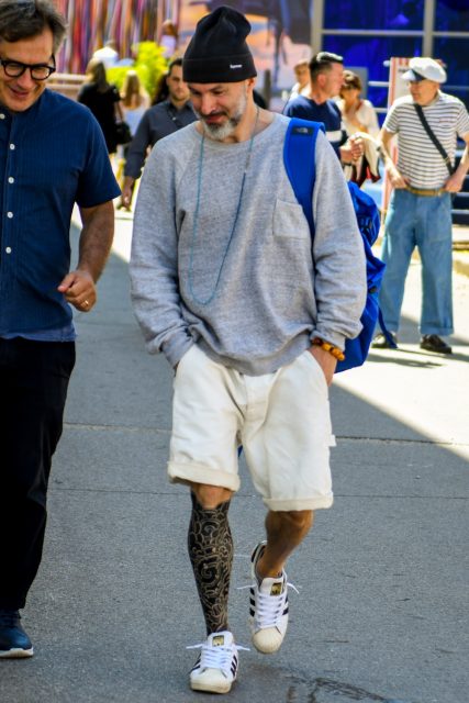 A men's oversized spring/summer outfit with a plain knit cap, plain gray sweatshirt, plain white shorts, and Adidas Superstar white low-cut sneakers.