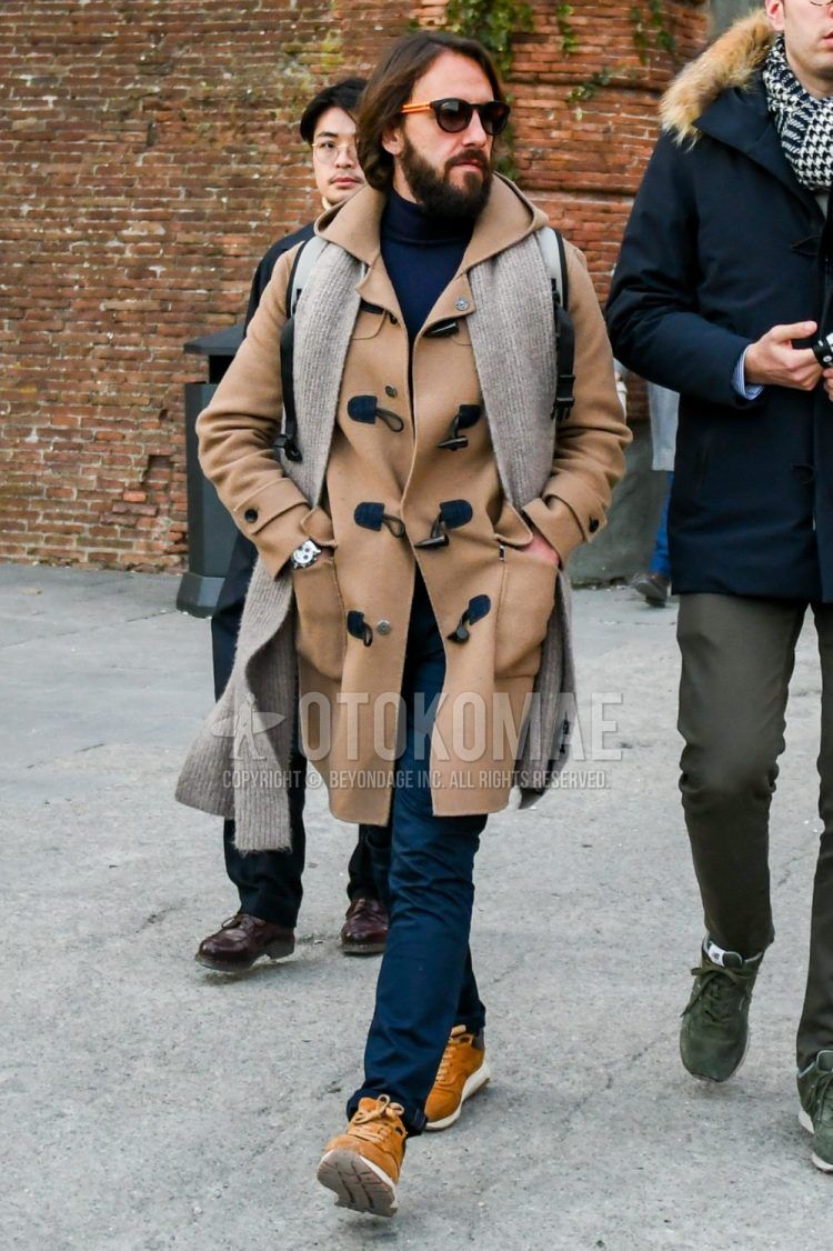 Wearing a men's fall/winter outfit with solid black/orange sunglasses, solid beige scarf/stall, solid beige duffle coat, solid navy turtleneck knit, solid navy chinos, and beige low-cut sneakers.