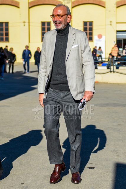 Fall and spring men's coordinate outfit with solid beige glasses, solid gray tailored jacket, dark gray solid turtleneck knit, solid gray wool pants, solid brown socks, and brown wingtip leather shoes.
